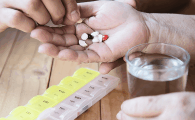 A person holding a handful of pills in one hand and a glass of water in the other, preparing to take medication.