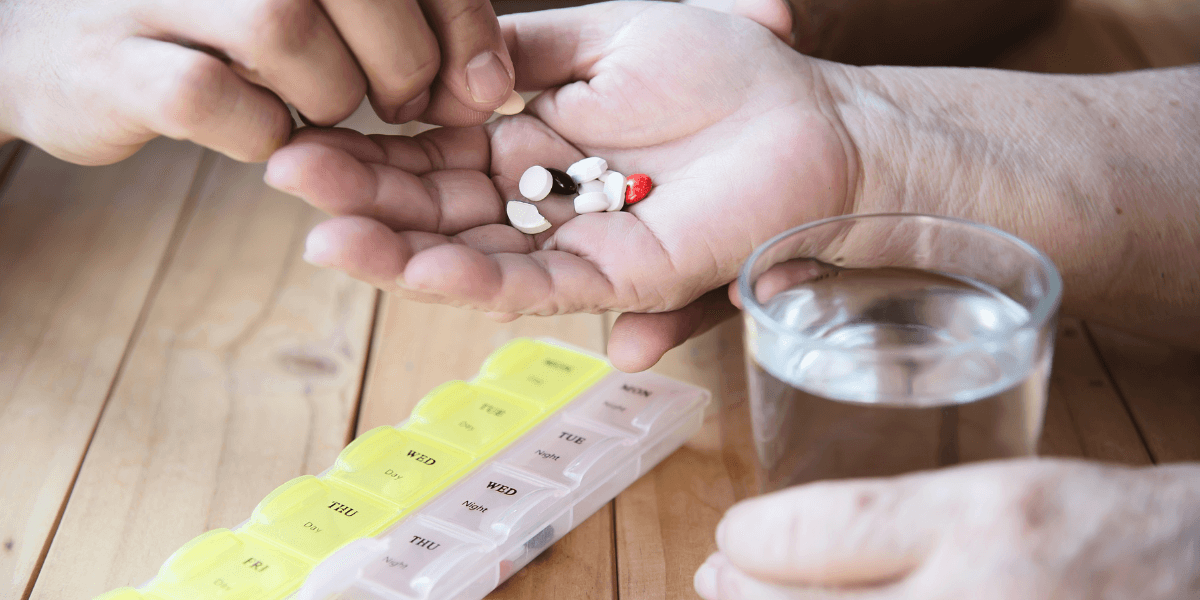 A person holding a handful of pills in one hand and a glass of water in the other, preparing to take medication.