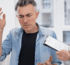 Middle-aged man looking unwell and touching his head while consulting a doctor who is holding a clipboard."